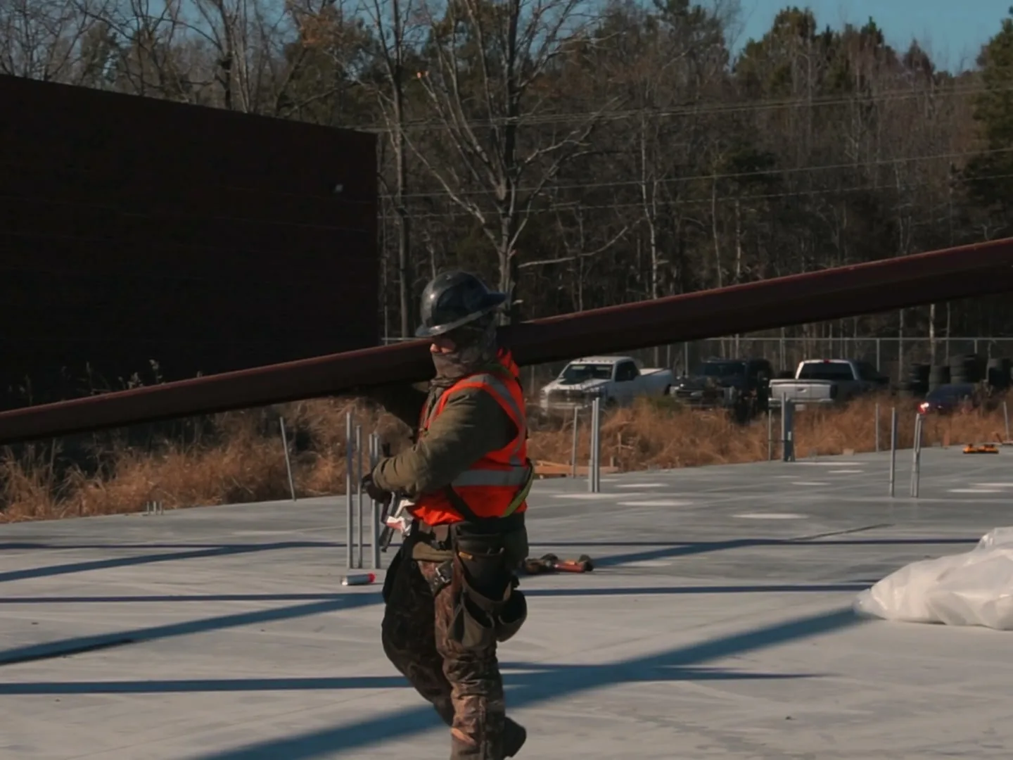 Ironworker carrying a steel beam across a new slab beside an existing building, commercial additions