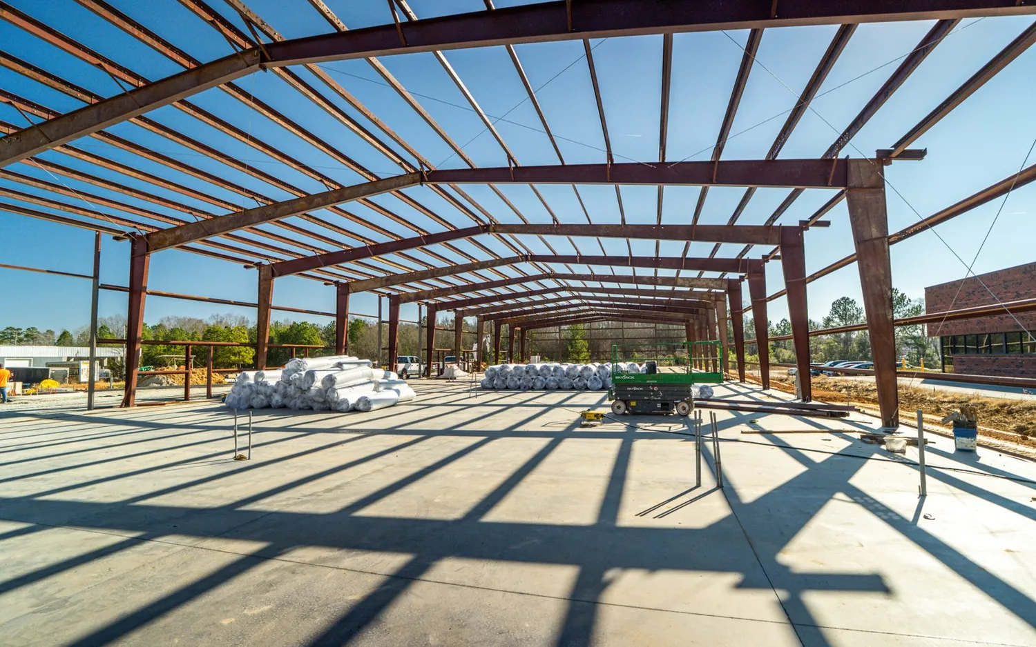 New steel building frame rising over a slab next to an existing brick building, commercial additions