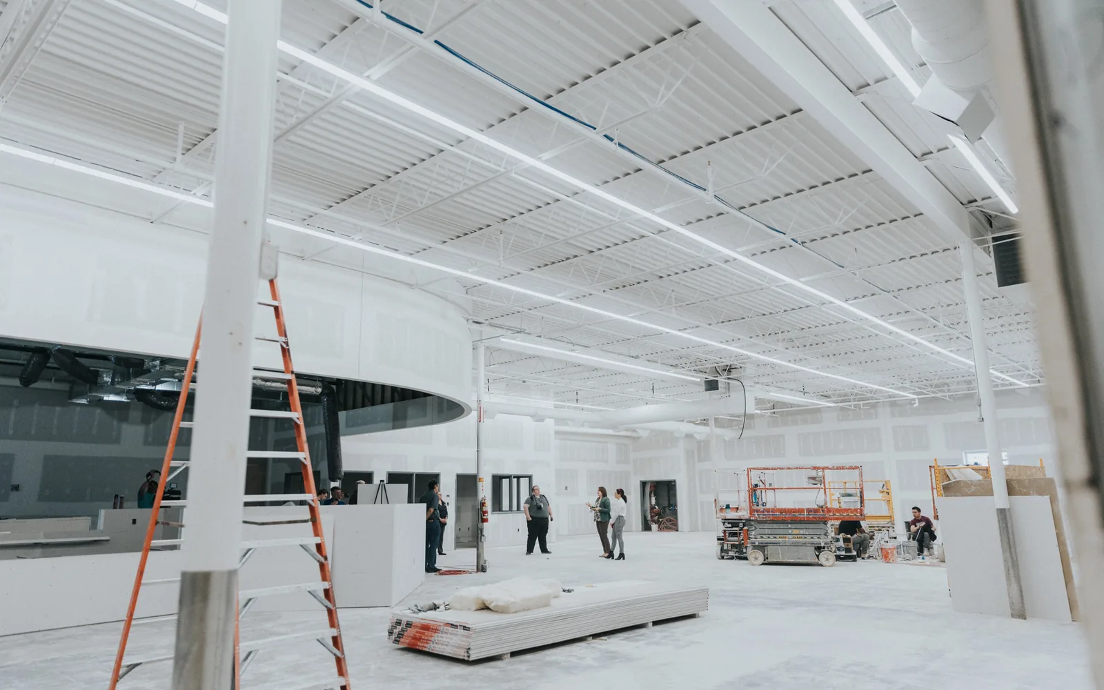 Large open span building mid renovation with new drywall walls, a curved soffit and a scissor lift, commercial remodeling