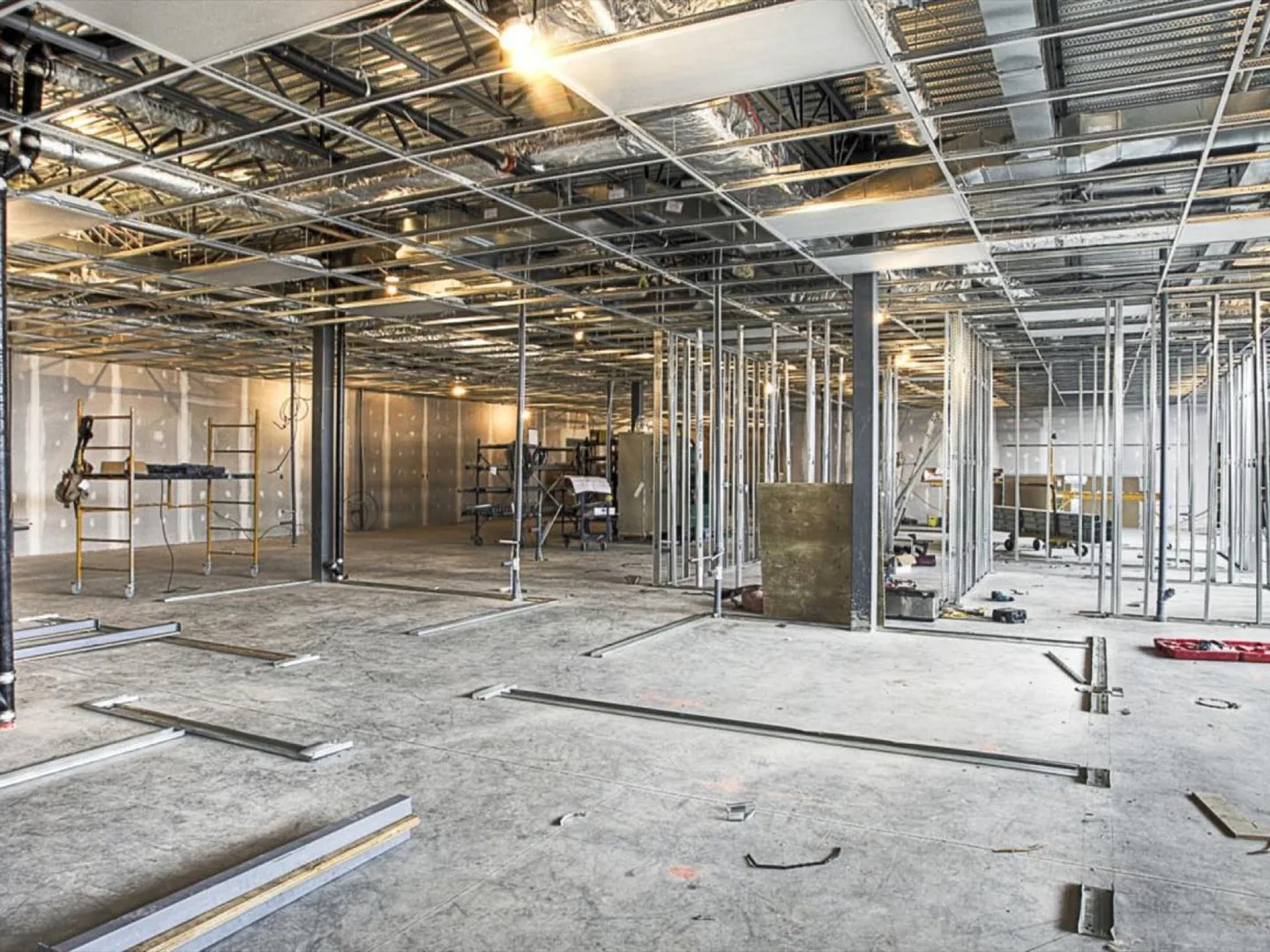 Commercial interior under renovation with metal stud partitions, an open ceiling grid, ductwork and rolling scaffolds, commercial remodeling