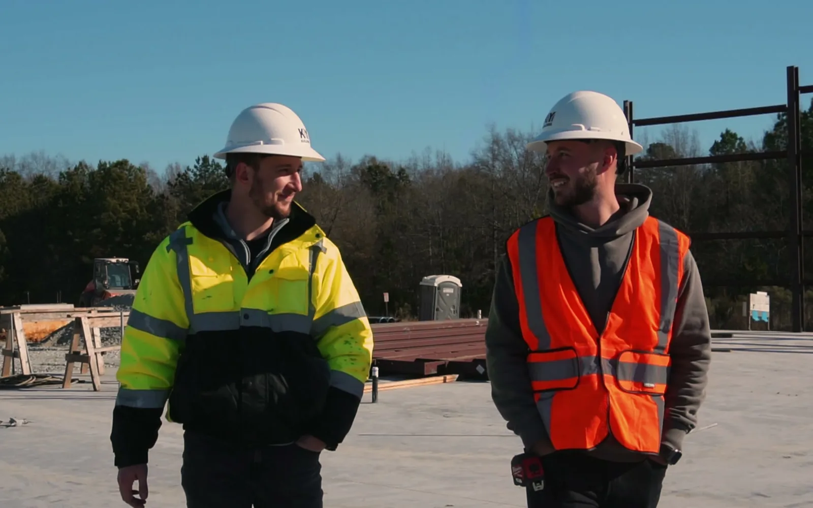Two builders in hard hats walking across a new concrete slab, design build