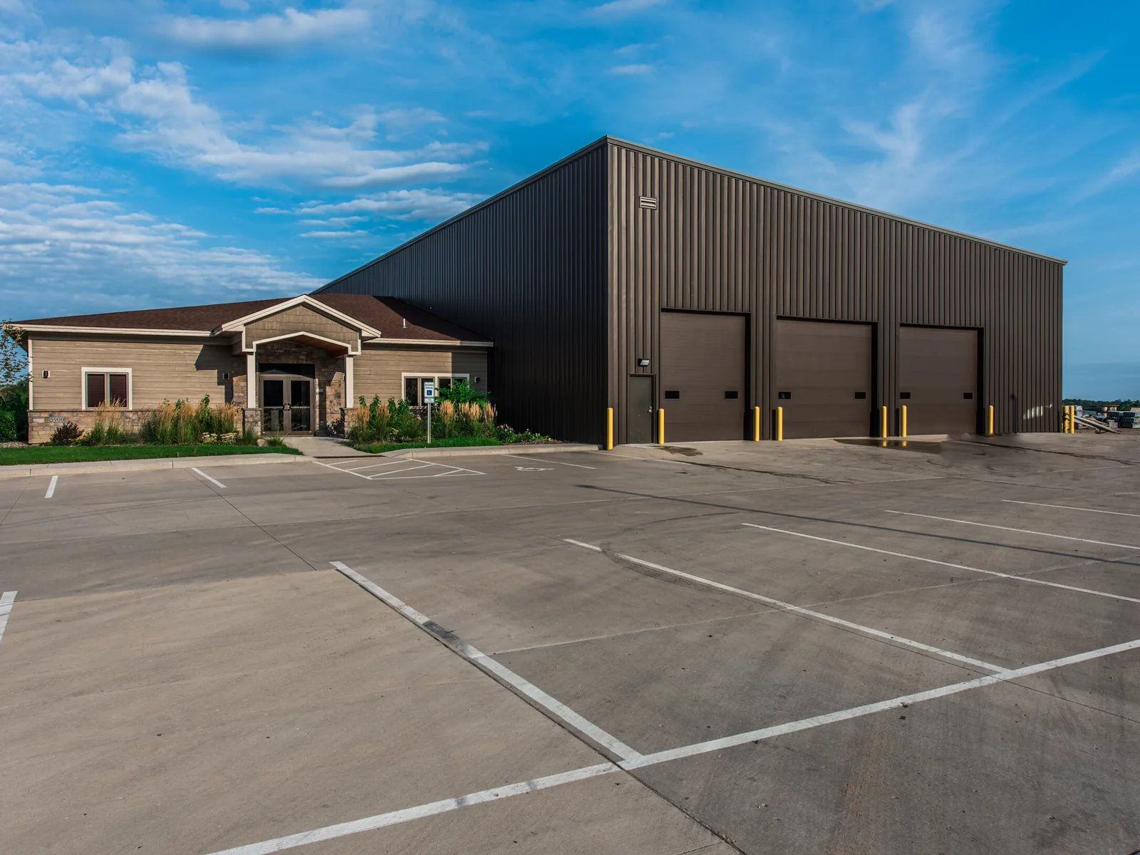 Finished dark brown metal warehouse with three overhead doors and a stone and siding office wing, design build