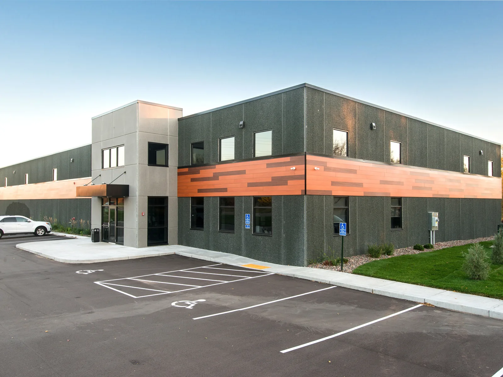 Finished two story office warehouse building with dark wall panels, a glass entry and a new parking lot, design build