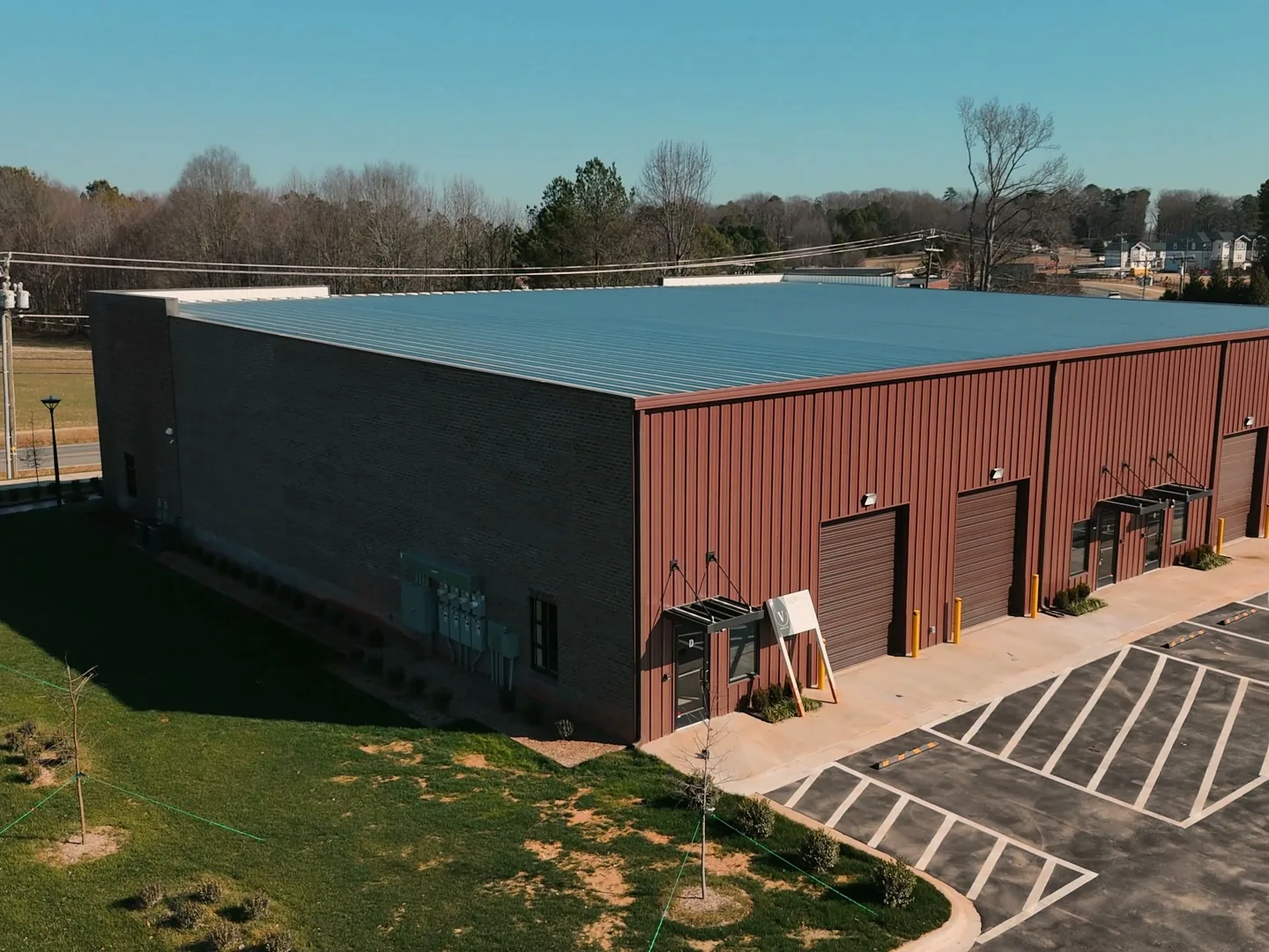 Aerial view of a finished dark red metal flex building with roll up doors and a striped parking lot, flex space construction