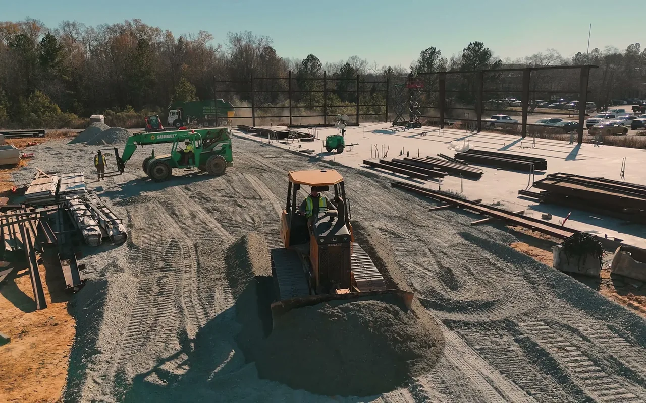 Dozer spreading stone across a new building pad with steel stacked nearby, ground up construction