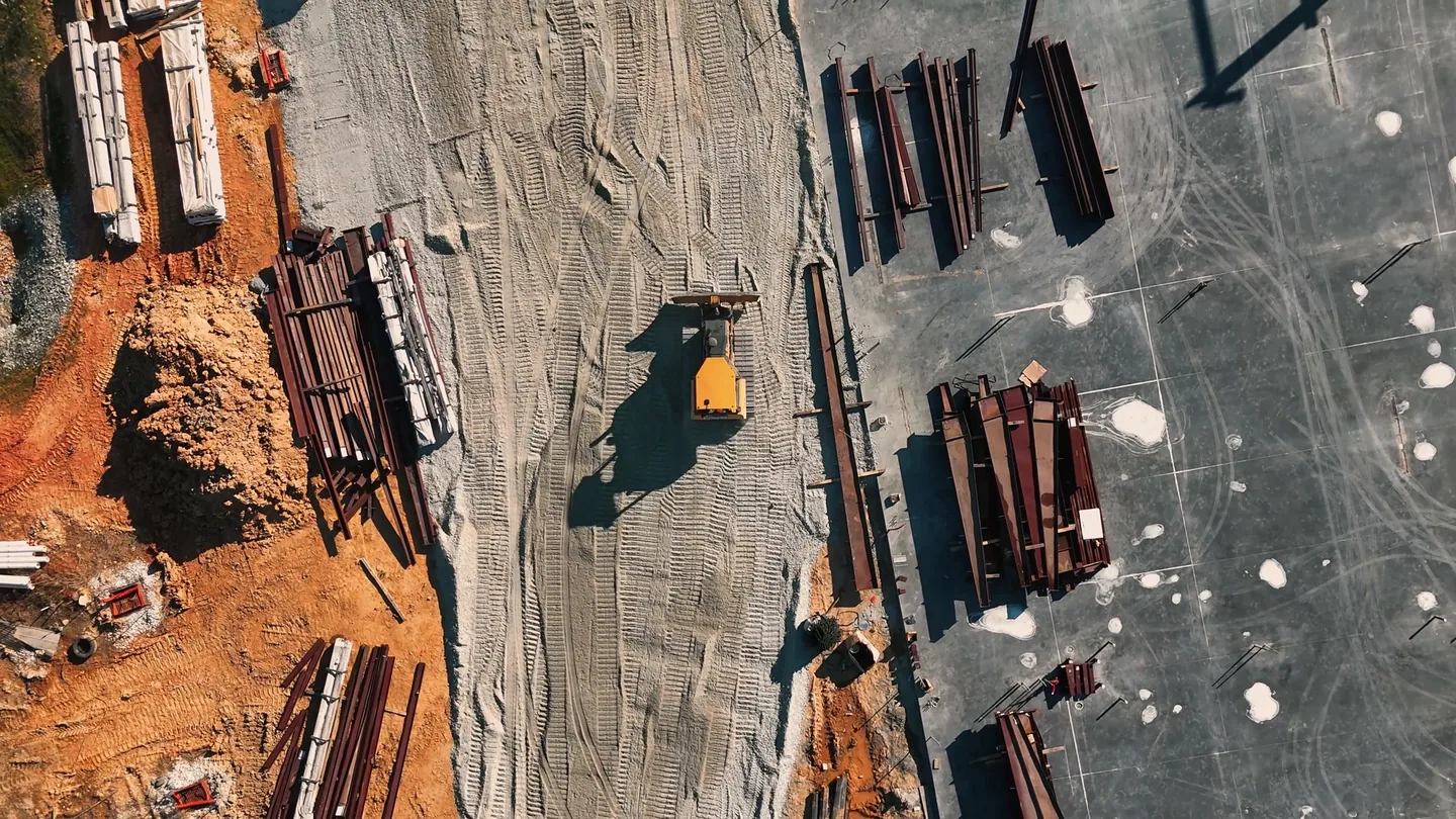Overhead view of steel members staged on red clay beside a new building pad, commercial general contractor