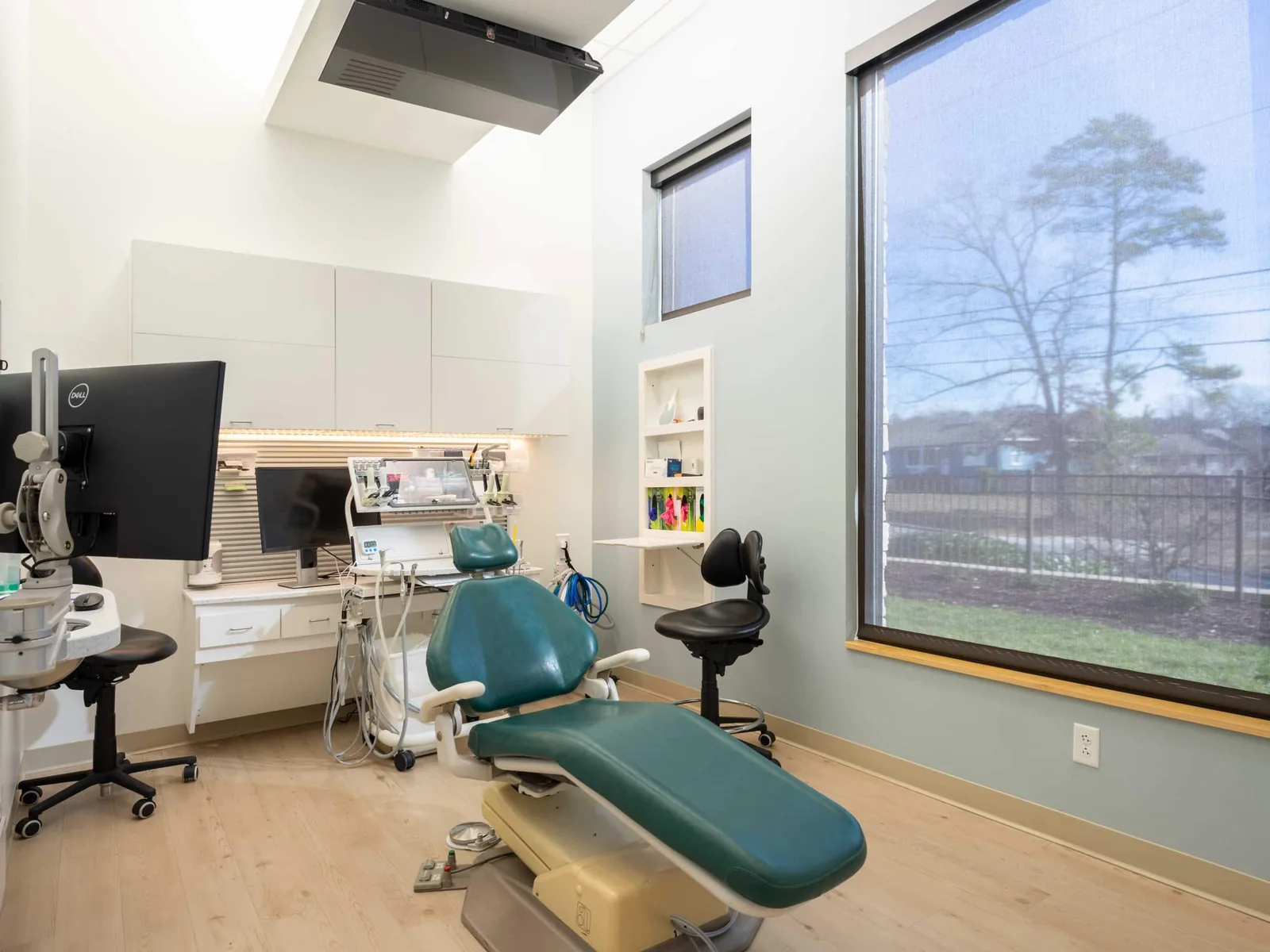 Finished dental treatment room with a dental chair, white cabinetry and a large window, medical office build outs
