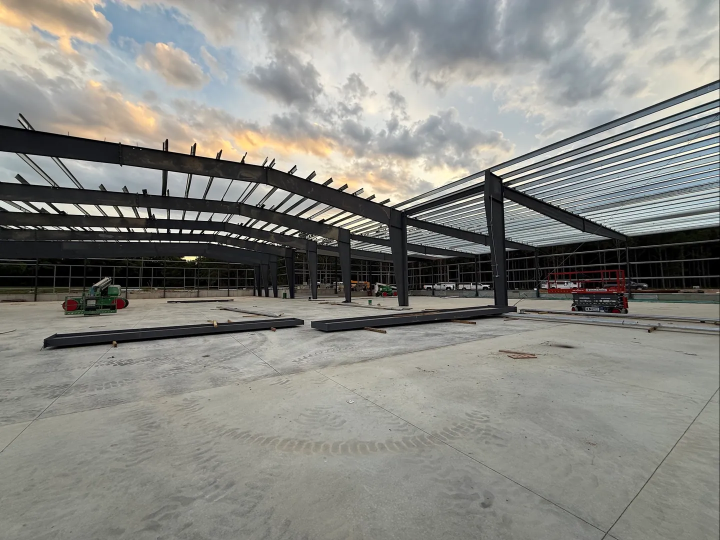 Steel rigid frames and purlins standing over a new concrete slab at dusk, metal building construction