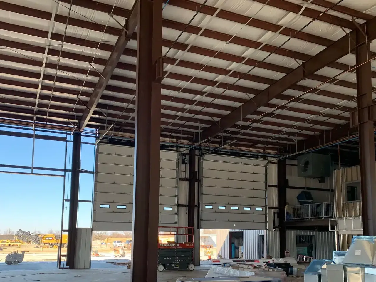 Inside a metal building shell with overhead doors and new office walls being framed, metal building construction