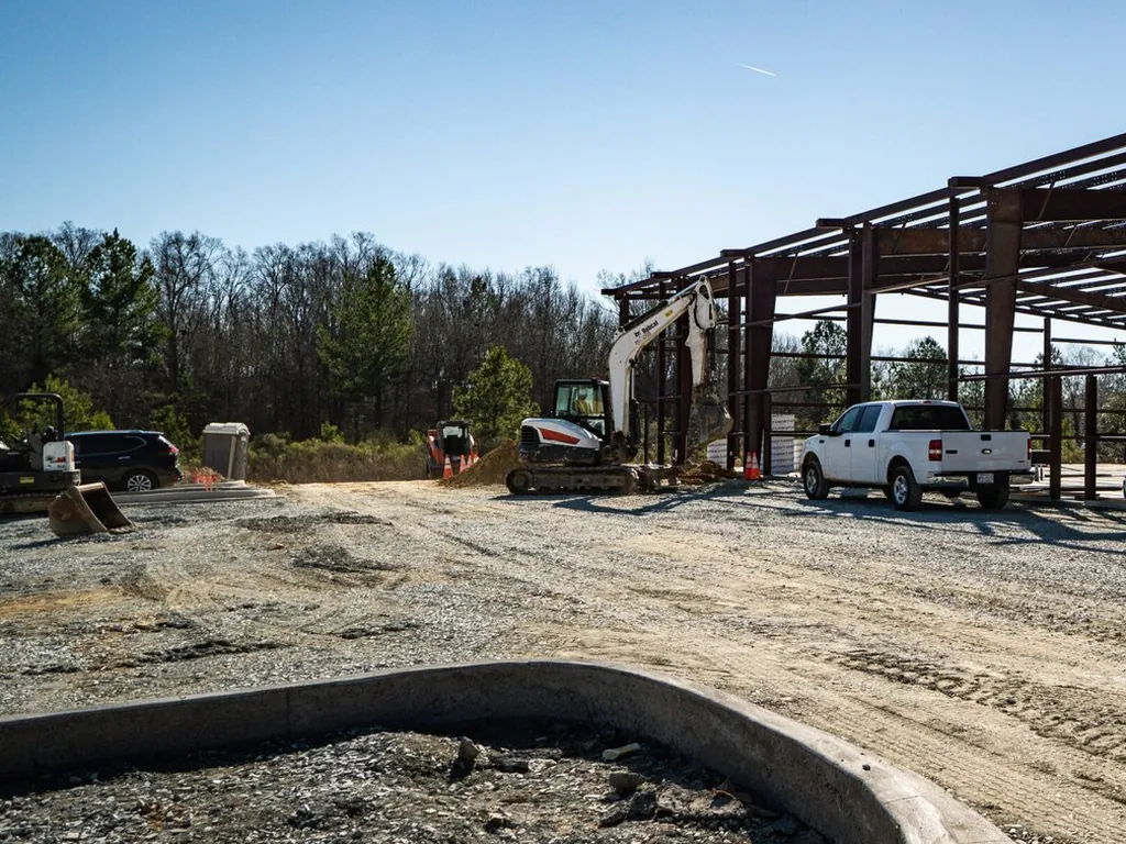 Red pre-engineered steel frame rising over a gravel site with a work truck parked below, metal building construction