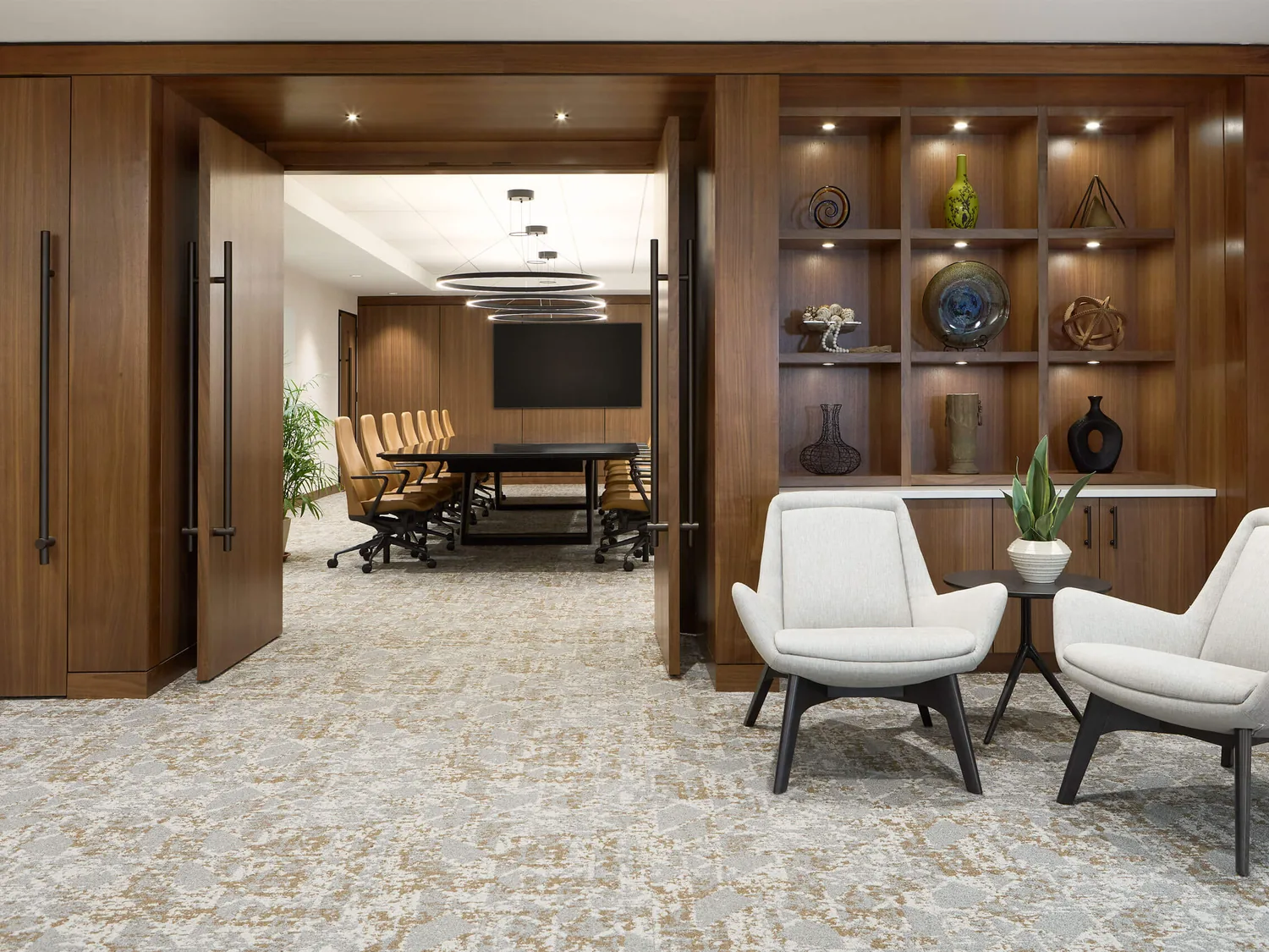 Renovated office lounge with walnut paneling and tall pivot doors open to a conference room, office renovation