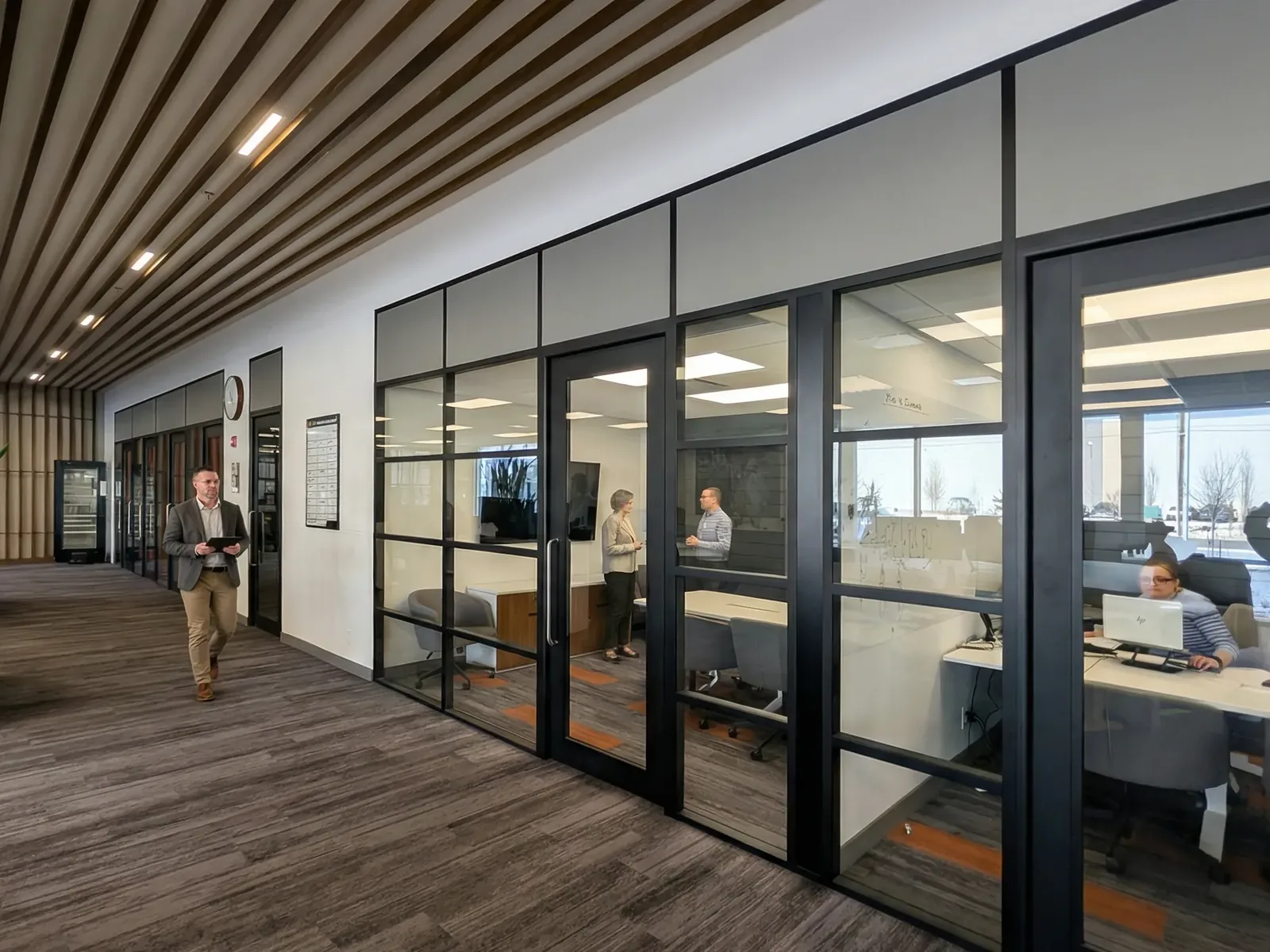 Office corridor with black framed glass office fronts, a wood slat ceiling and carpet, office renovation