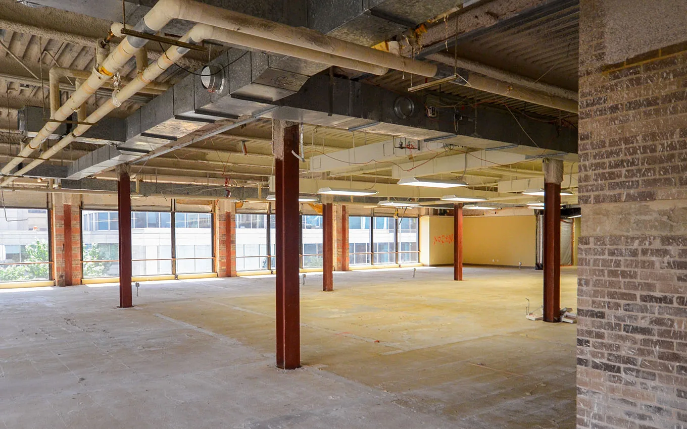 Office floor stripped to the shell for renovation with a bare slab, exposed ducts and steel columns, office renovation