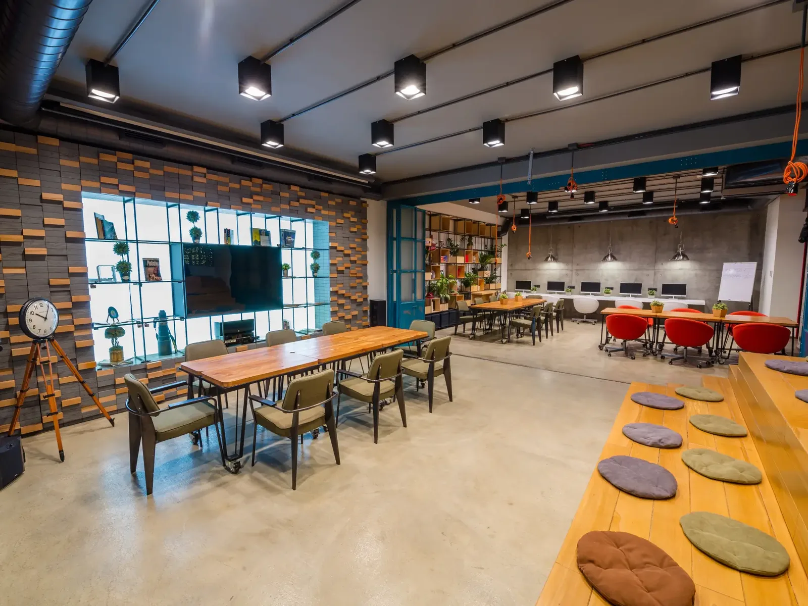 Open plan office with long work tables, red task chairs and black pendant lights, office renovation