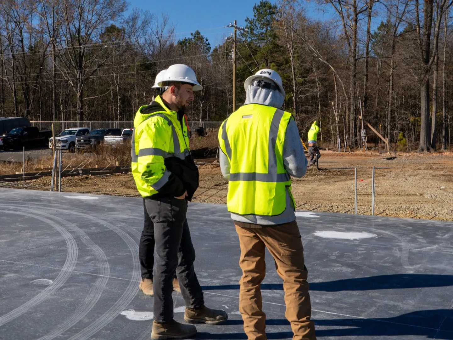 Two builders in safety vests talking on a new slab beside a cleared site, preconstruction