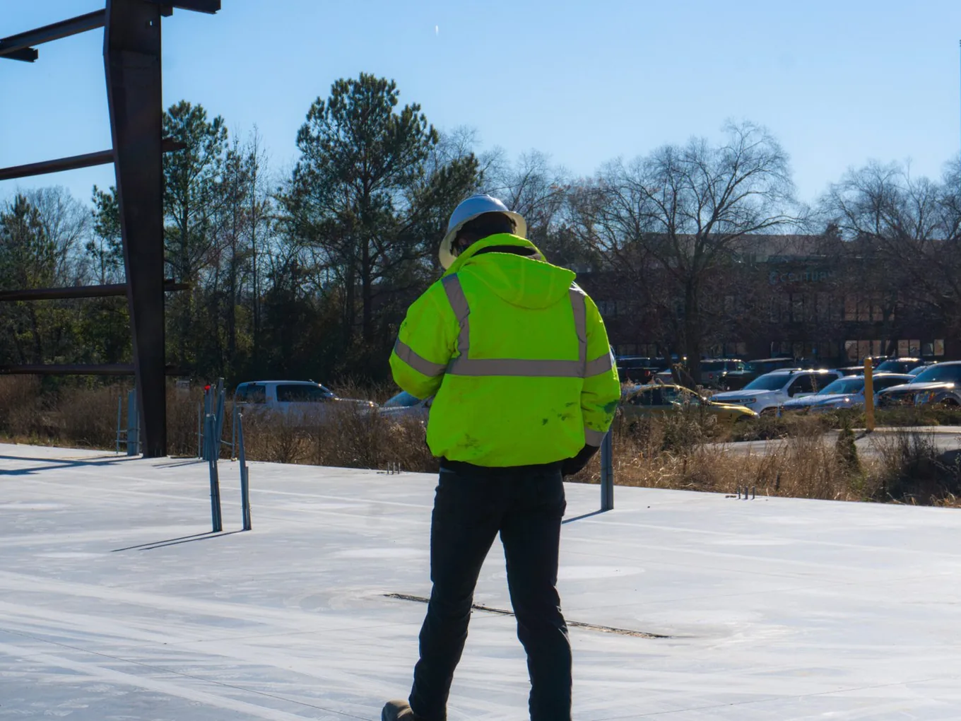 Builder in a safety jacket looking over a new slab toward the parking lot, preconstruction