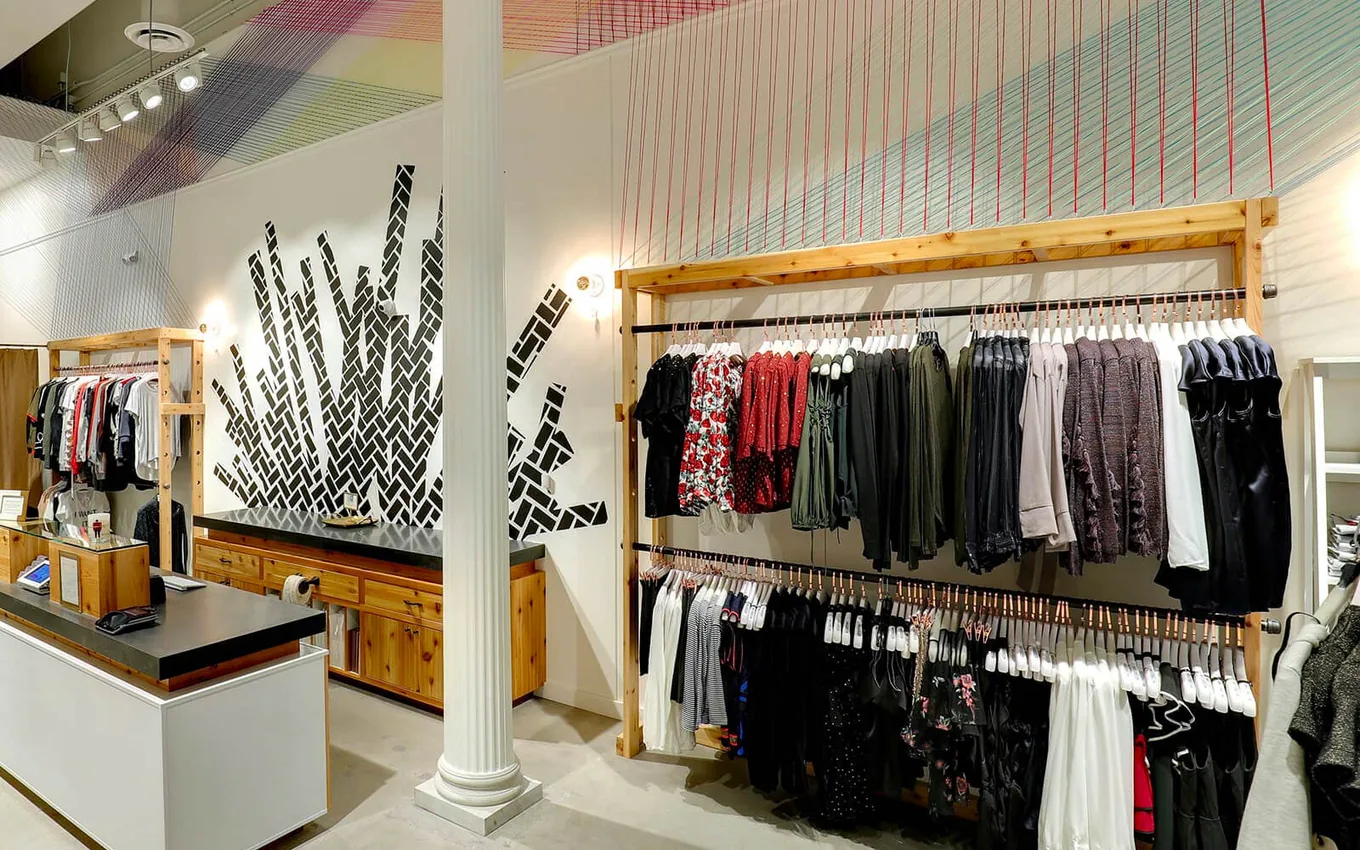 Finished boutique store interior with wood clothing racks, a cash wrap counter and a tile mural wall, retail build outs