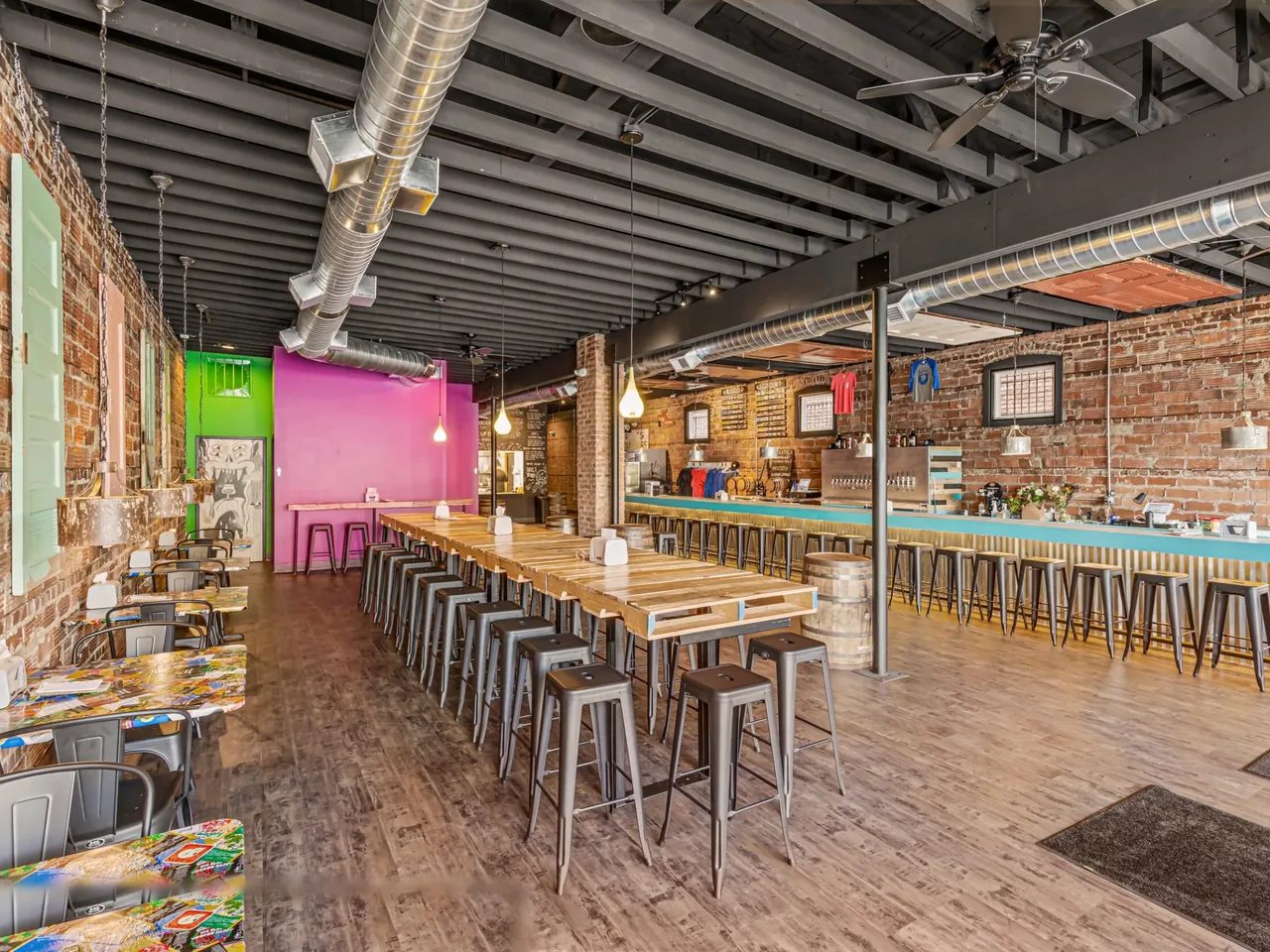 Finished taproom restaurant in a brick storefront building with a long bar, communal tables and exposed ductwork, retail build outs