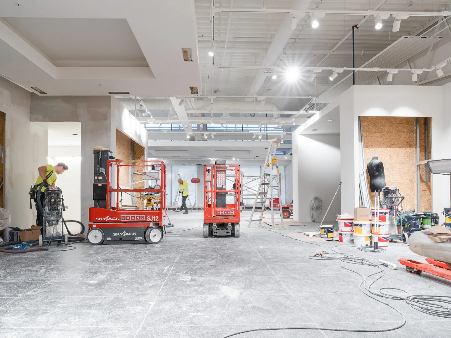 Retail store interior mid build out with scissor lifts, sheathed walls, new soffits and track lights, retail build outs