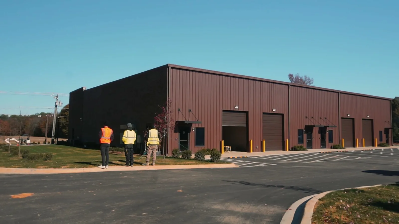 Three people walking toward a finished dark red metal flex building, commercial general contractor