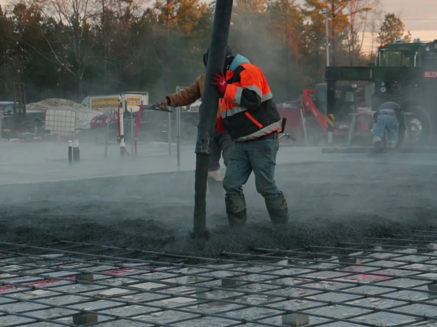 Crew pouring a concrete slab over rebar mesh on a cold morning, warehouse construction