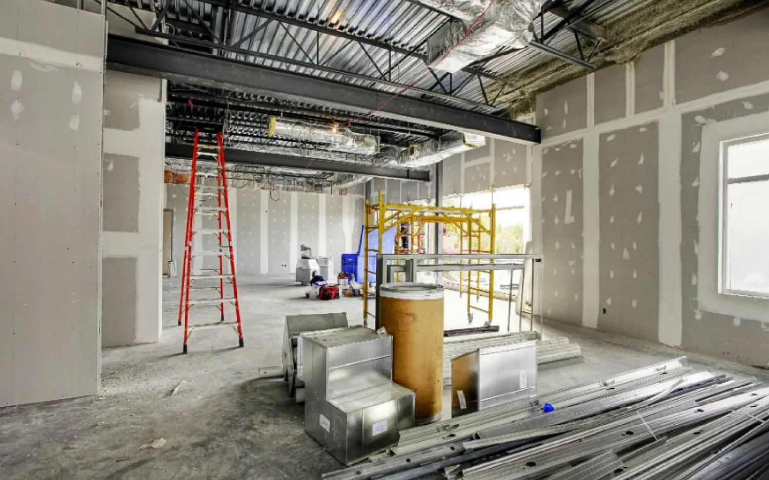 Interior build out in progress under steel joists and metal deck with taped drywall walls and new ductwork, warehouse renovation