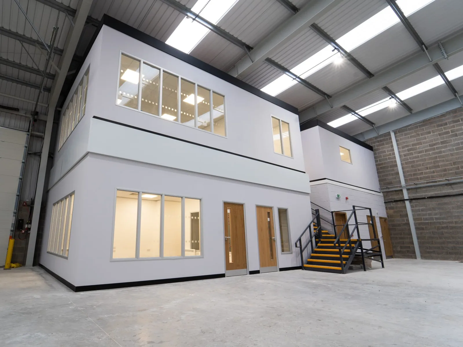 Two story office block built inside a warehouse with a steel stair beside an overhead door, warehouse renovation