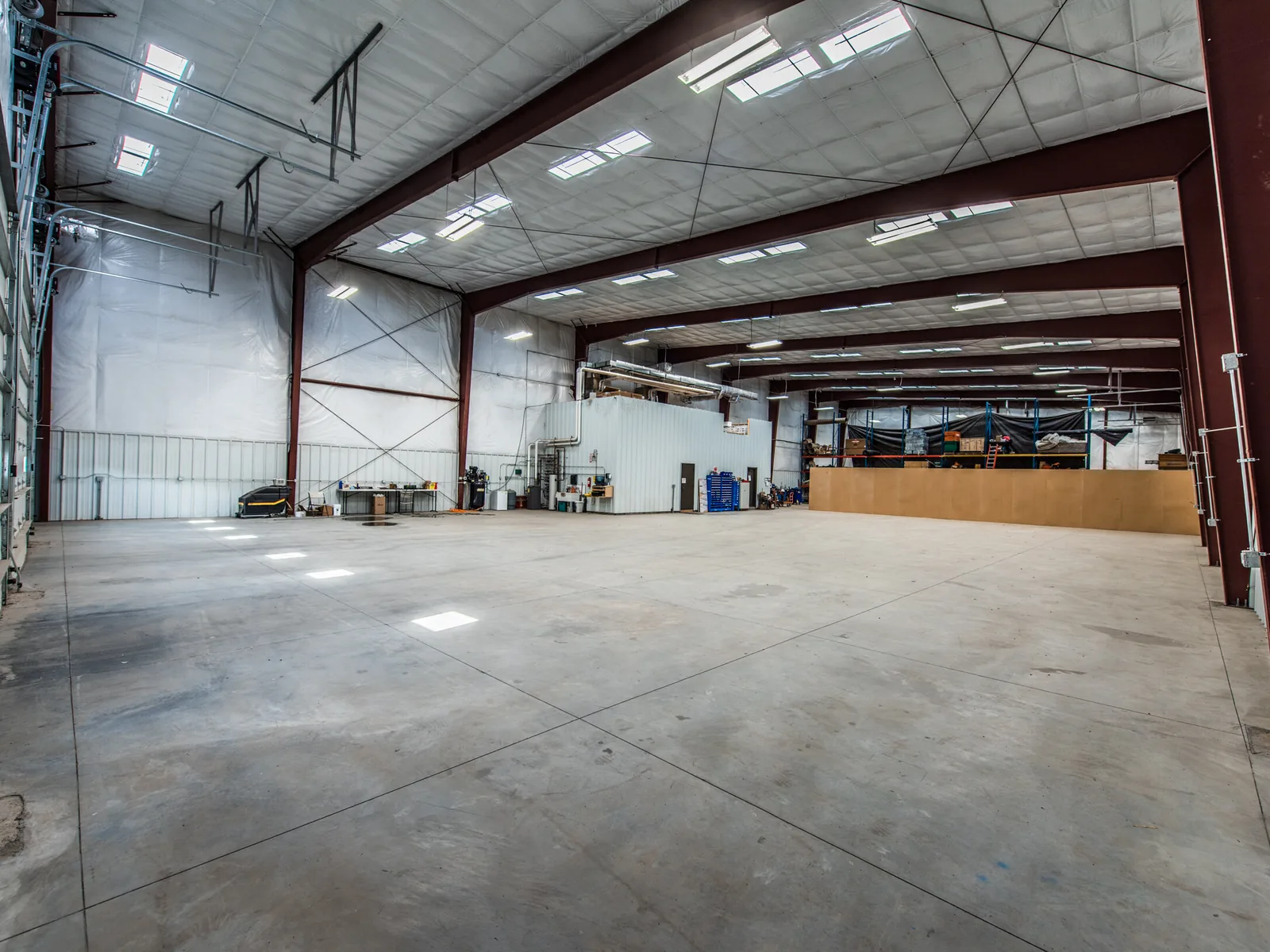Open metal warehouse interior with steel frames, white insulated walls, a concrete floor and skylights, warehouse renovation